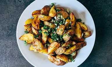 Crispy roasted potato wedges sprinkled with fresh chopped herbs on a white round plate.