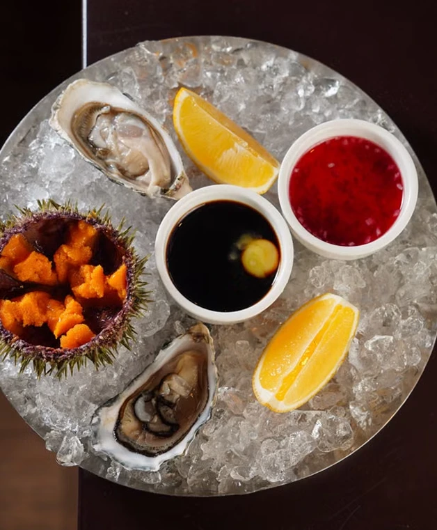 Top-down view of fresh raw oysters served on ice with lemon wedges and dipping sauces.