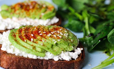 Two slices of toasted bread topped with cottage cheese, sliced avocado, and red pepper flakes.