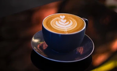 Hot cappuccino with leaf latte art served in a dark blue ceramic cup on a saucer.