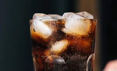 A glass filled with ice cubes and dark soda drink garnished with a slice of fresh lime.
